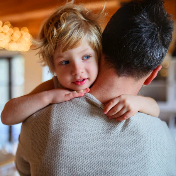 Adoptive daughter lovingly hugging her adoptive father in the kitchen while she looks out the window in wonder.