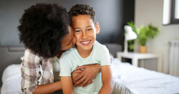 A Foster care child with foster parent enjoying a loving hug with a peck on the cheek.