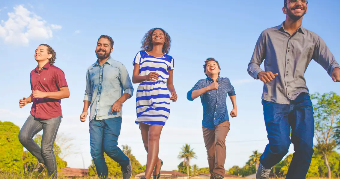 A group of Diverse foster care parents running and smiling in the park.