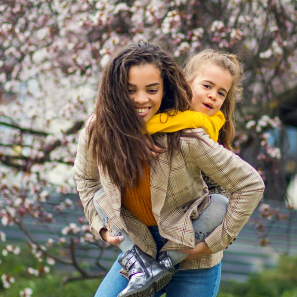 Foster parent giving her foster care child a piggy back ride in the park.