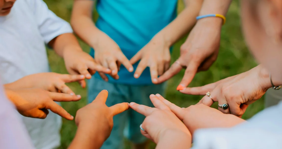 Kids playing in a circle with their fingers connecting in the middle.