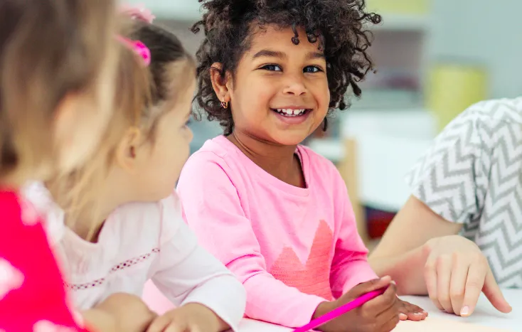 A child with autism coloring on a piece of paper in a classroom with other foster care children.